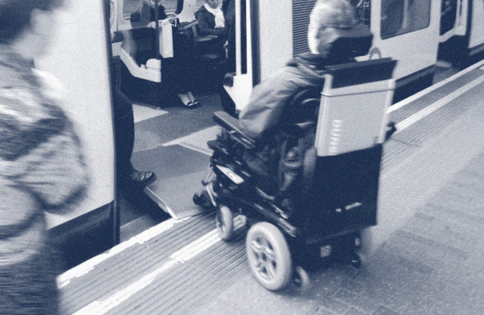 A wheelchair user boarding a London Underground train using a manual boarding ramp, with station staff assisting.